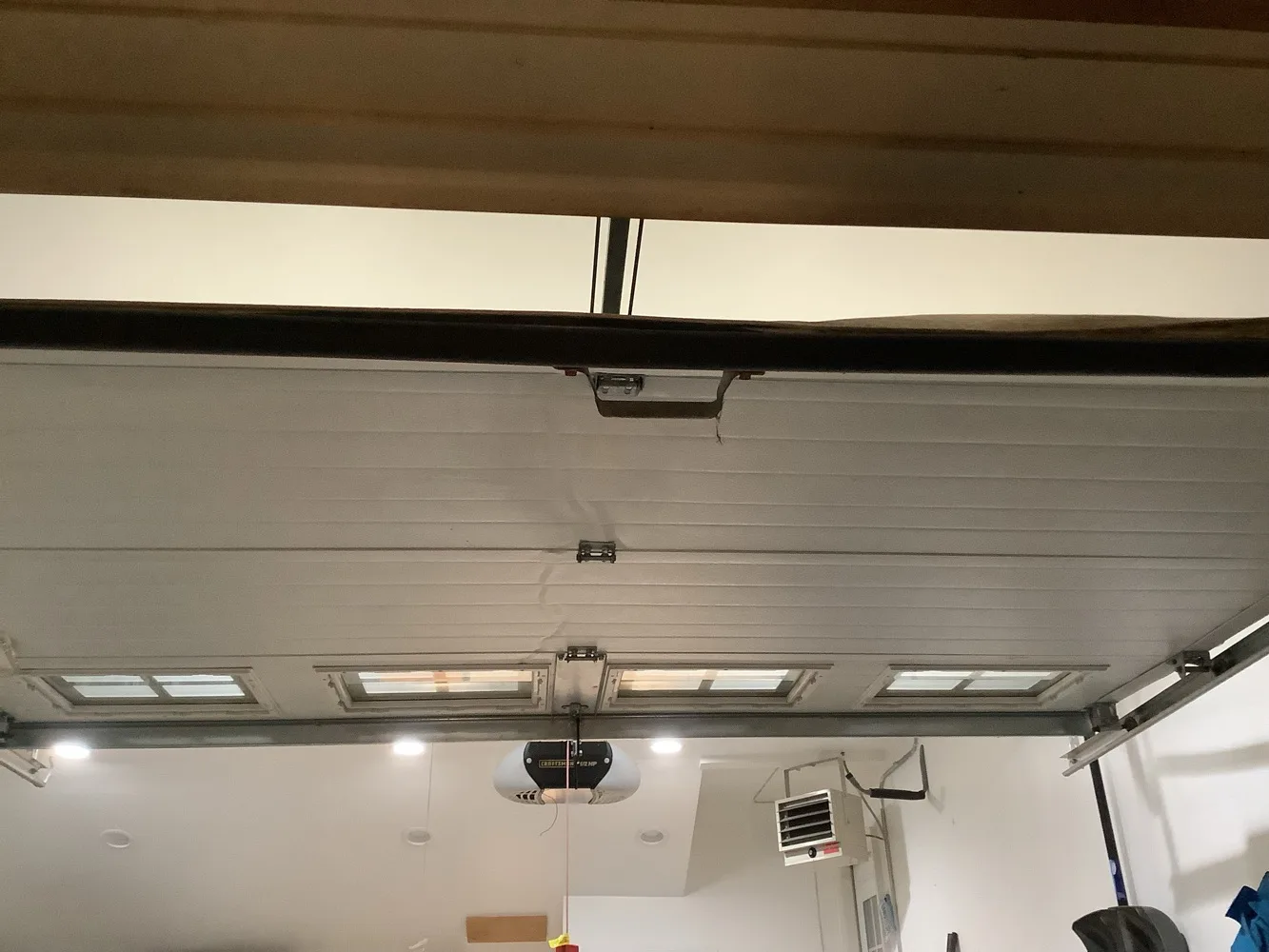 Sectional garage door raised flat onto its horizontal tracks overhead, its row of glazed lights facing down, with the opener motor and a ceiling heater visible beyond